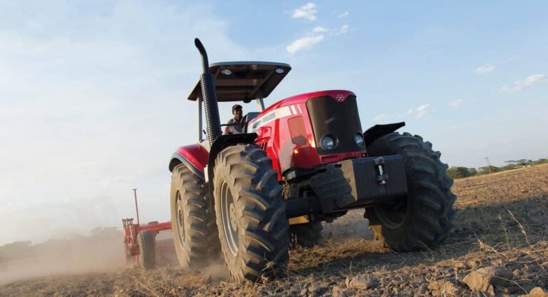 Red tractor ploughing dry field at sunset