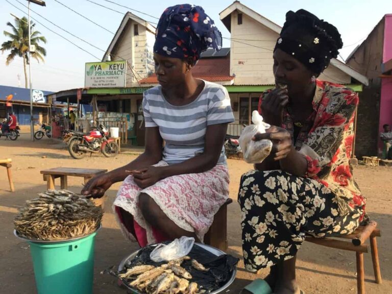 Two women selling and eating dried fish outdoors