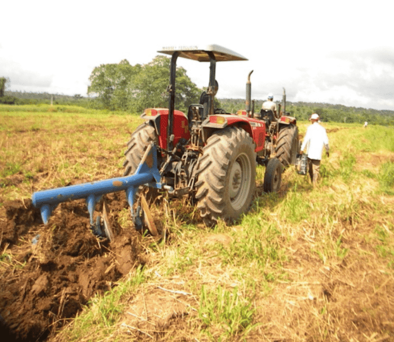Red tractor ploughing field with farmer walking beside