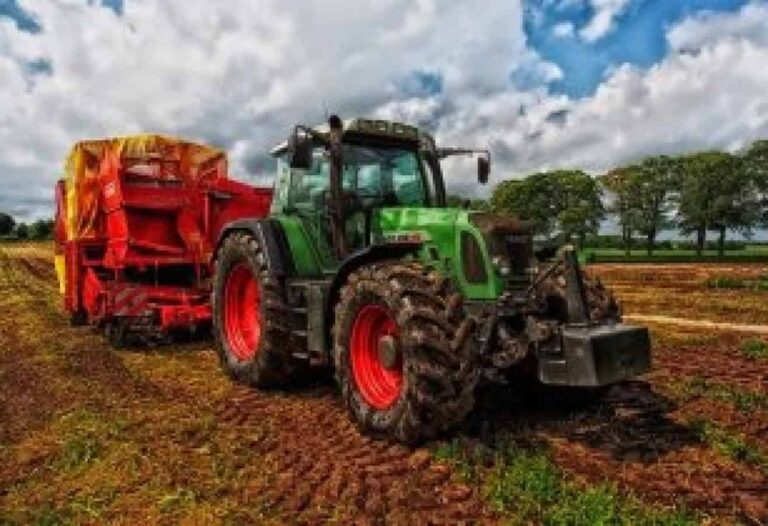 Green tractor towing red trailer across field