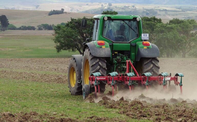 Green tractor ploughing field in countryside