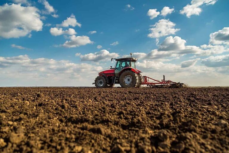 Red tractor ploughing field under blue sky