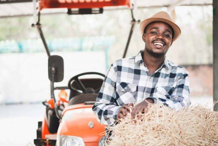 Smiling farmer leaning on hay bale by tractor