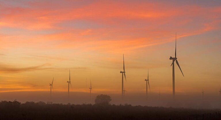 Wind turbines at misty sunset landscape