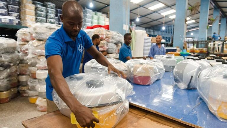 Workers wrapping large plastic containers in warehouse