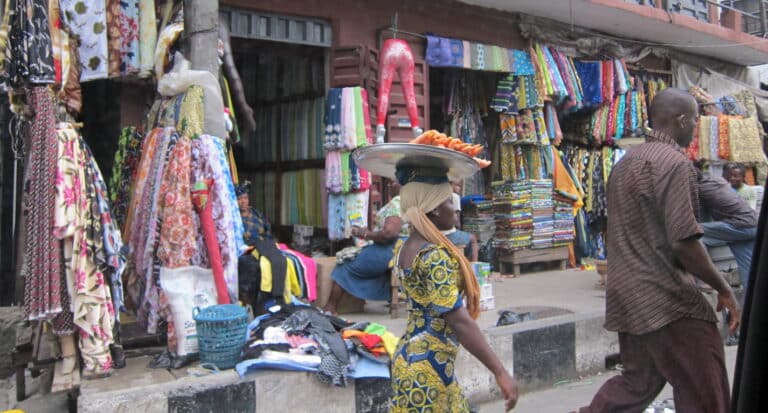 Woman carrying tray past colourful fabric market stalls