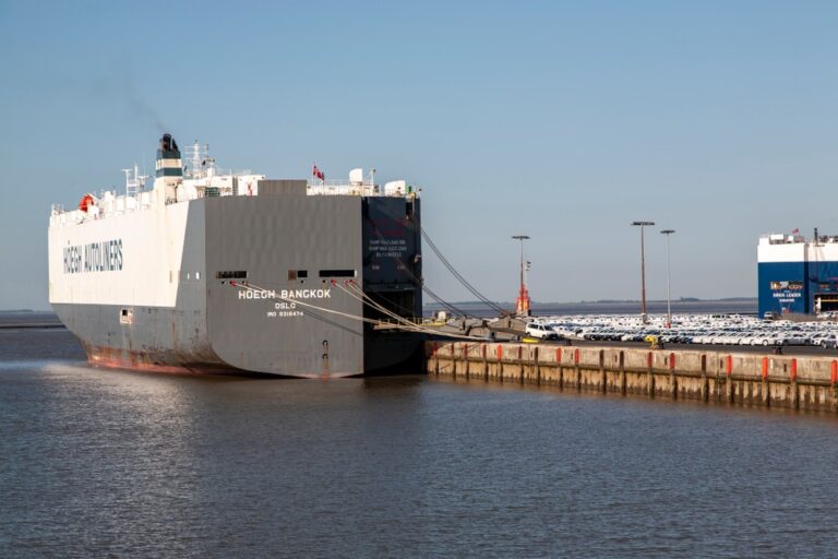 Car carrier ship docked beside rows of cars