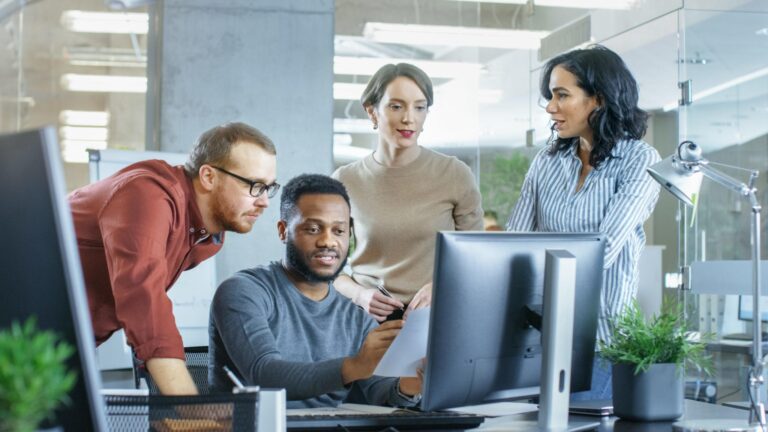 Four colleagues collaborating at computer in modern office
