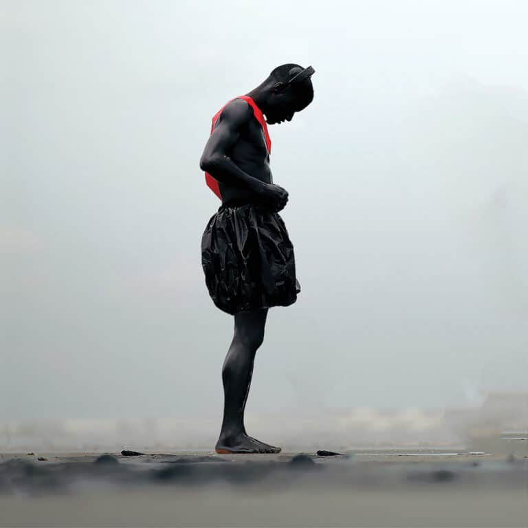 Person in black paint wearing red suspenders on beach