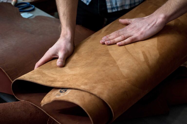 Hands inspecting sheet of brown leather on workbench
