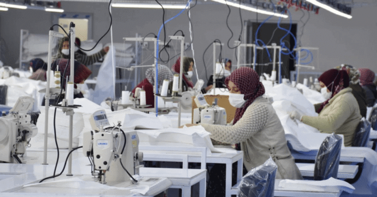 Factory workers sewing white garments at machines